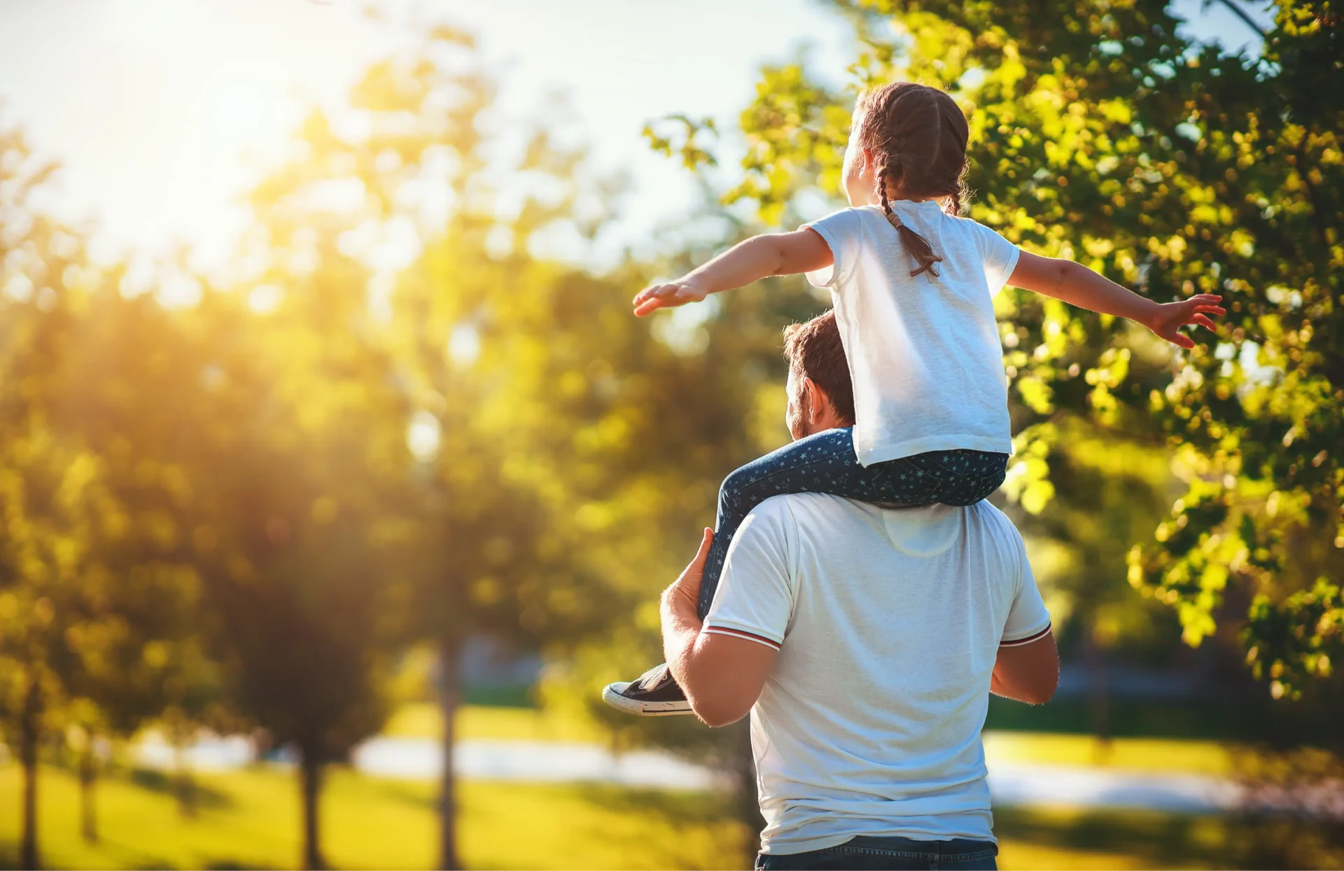 Father carrying daughter outdoors in park.