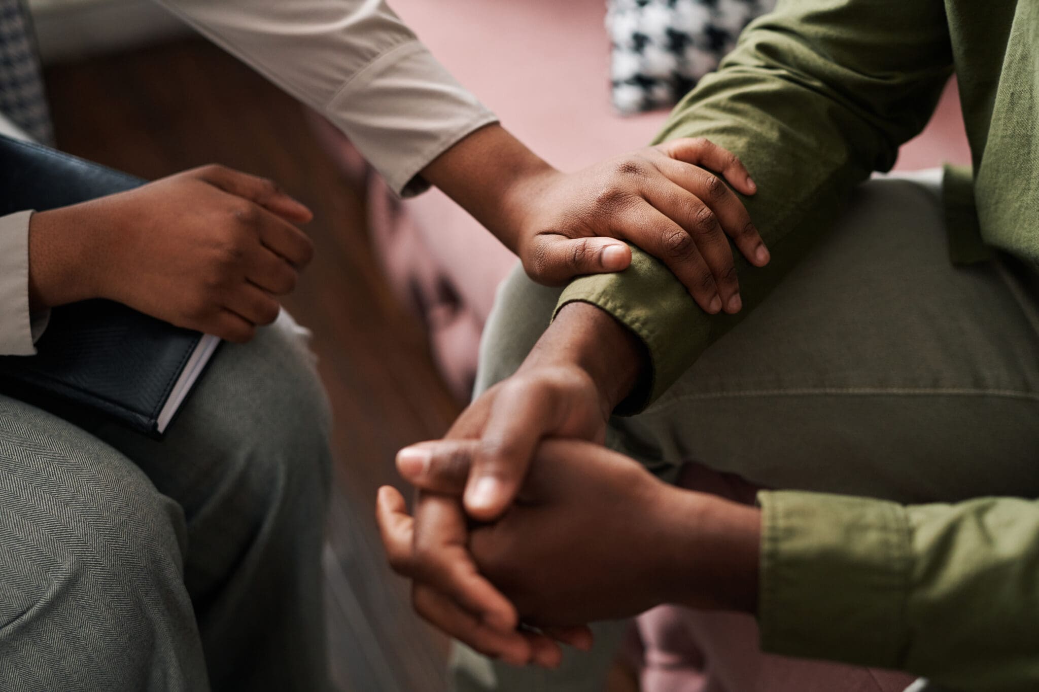 Young African American female psychologist keeping hand of wrist of male patient One person is comforting another with mental health issues.