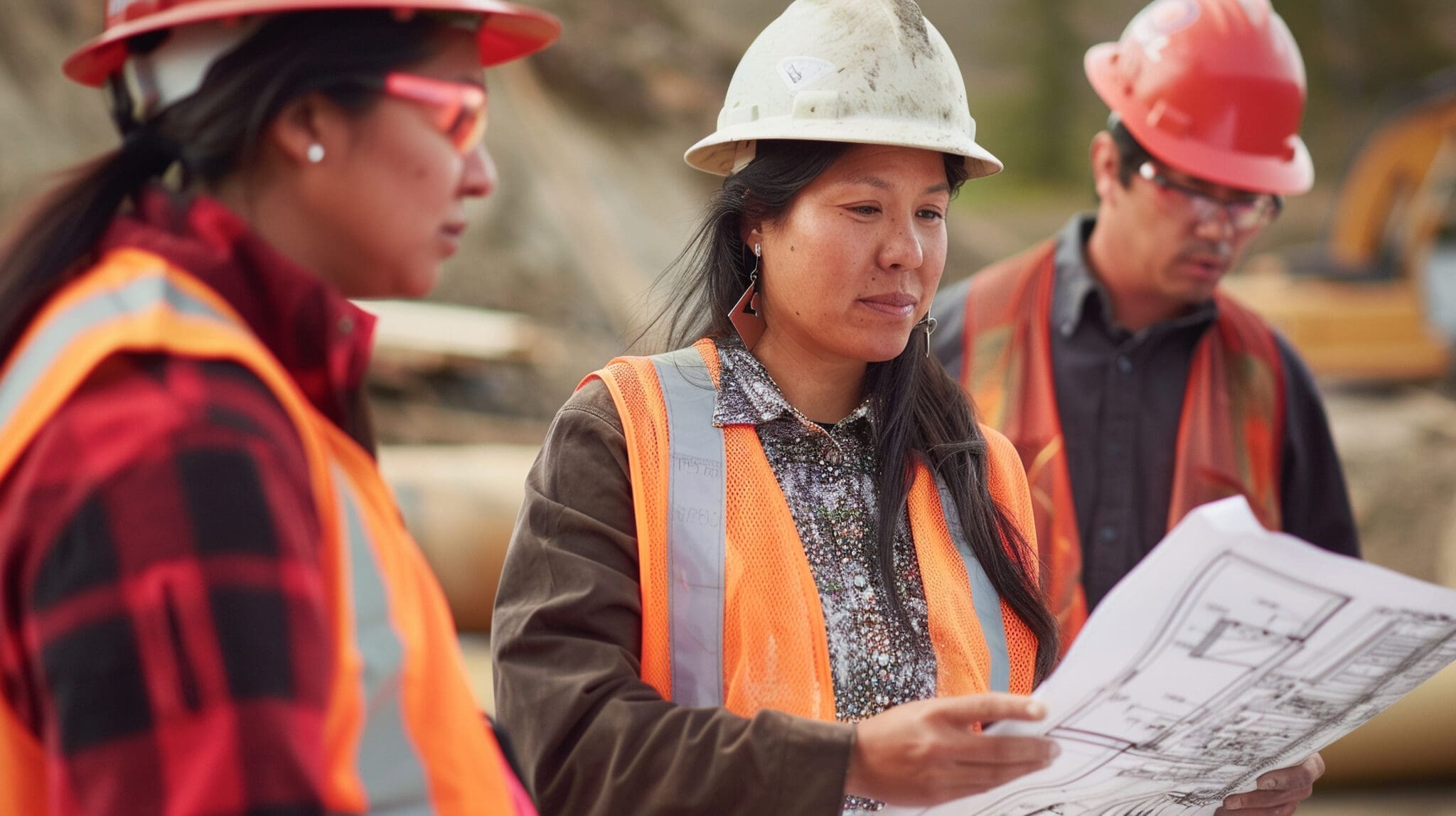 Indigenous woman engineer on a construction site, reviewing blueprints with colleagues Indigenous peoples working at a construction site.