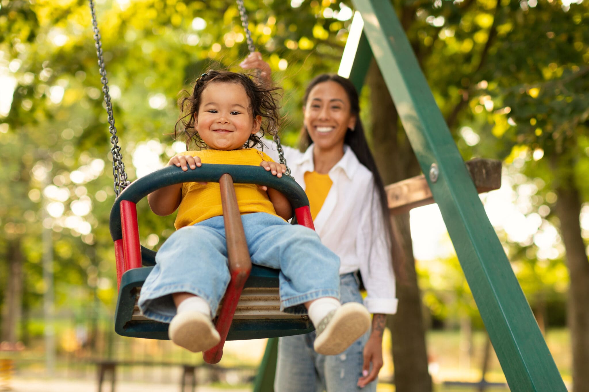 Smiling Korean Mother Swinging Baby On Swing On Playground Summer break with family.
