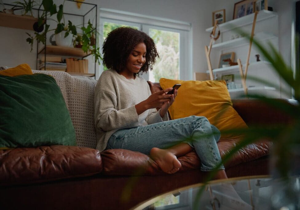 Happy young african woman using mobile phone while sitting a couch at home FIFO couple messaging each other to stay connected.