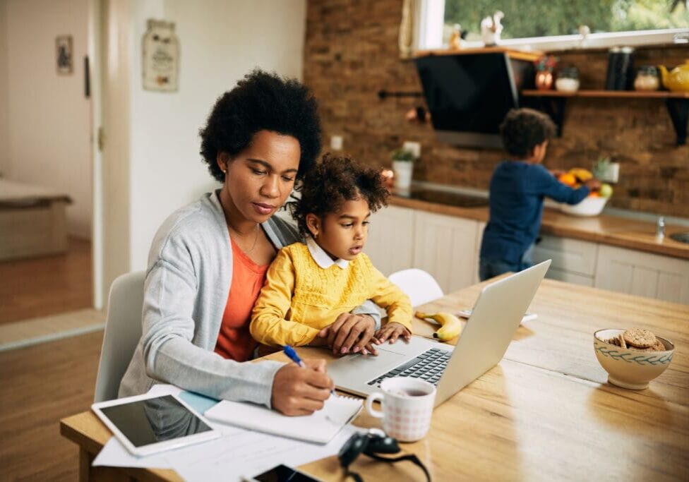 African American single mother with two kids working at home. Mother solo parenting with child in lap.
