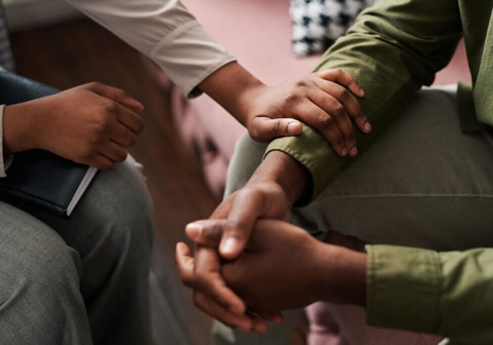 Young African American female psychologist keeping hand of wrist of male patient One person is comforting another with mental health issues.